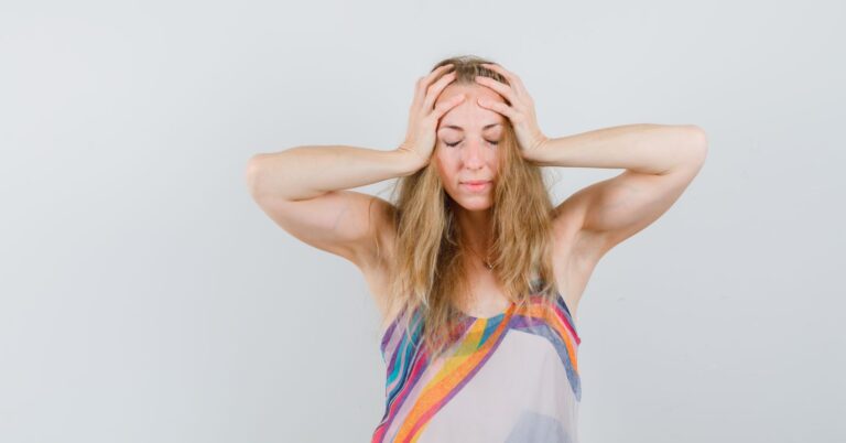 blonde lady summer dress clasping head with hands looking tired